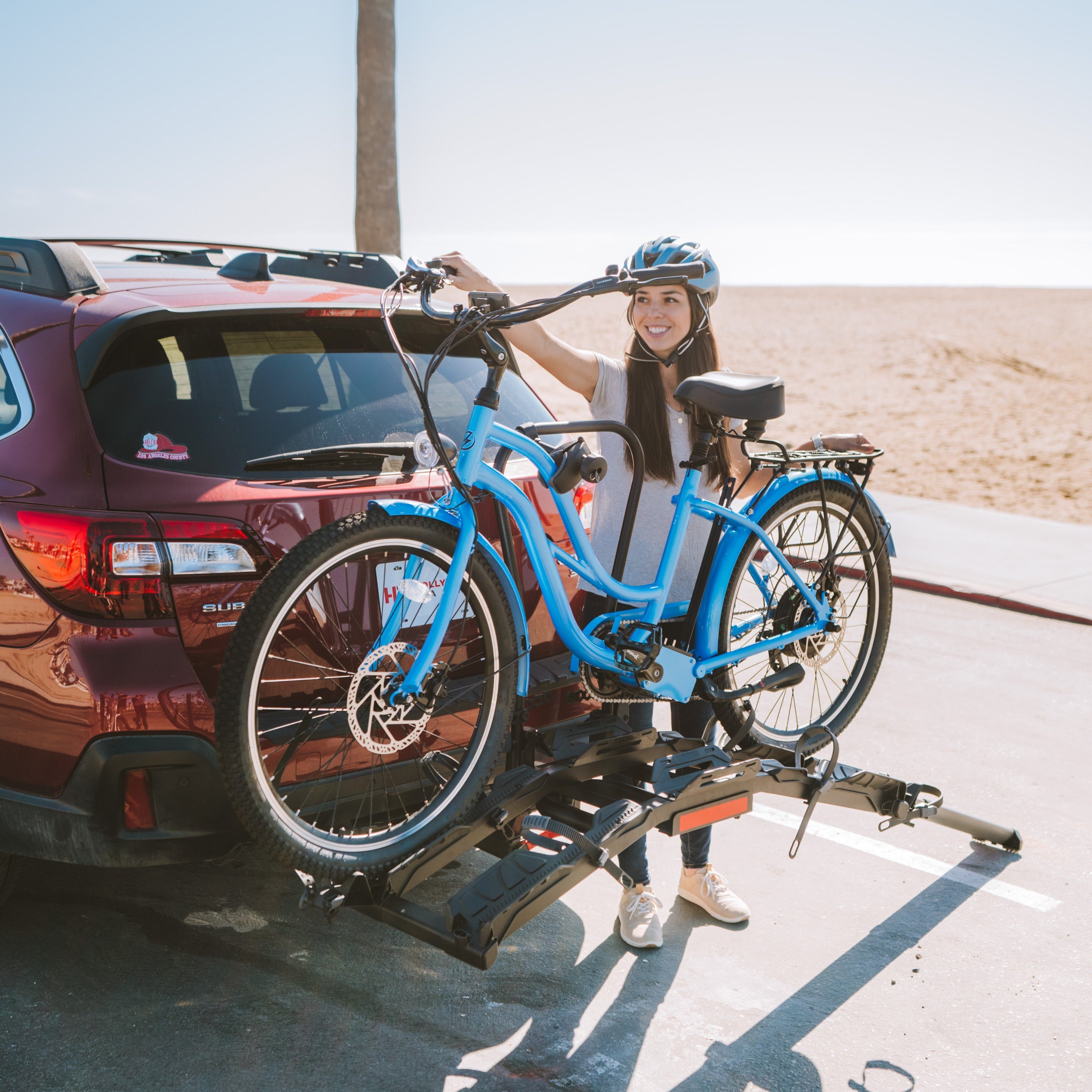 Woman loading blue electric bike onto Destination E hitch rack at the beach