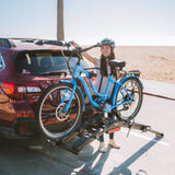 Woman loading blue electric bike onto Destination E hitch rack at the beach