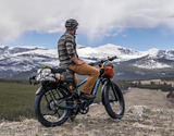 Velotric Nomad 2X Fat Tire Ebike showcasing its unbeatable payload capacity with a rider and extensive gear loaded on the rear rack, set against a mountain backdrop
